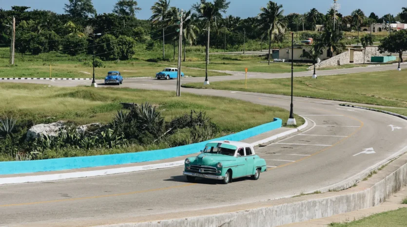Cars driving along a Cuban road between palm trees and green fields