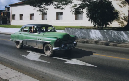 Green classic car driving down a street under a blue sky
