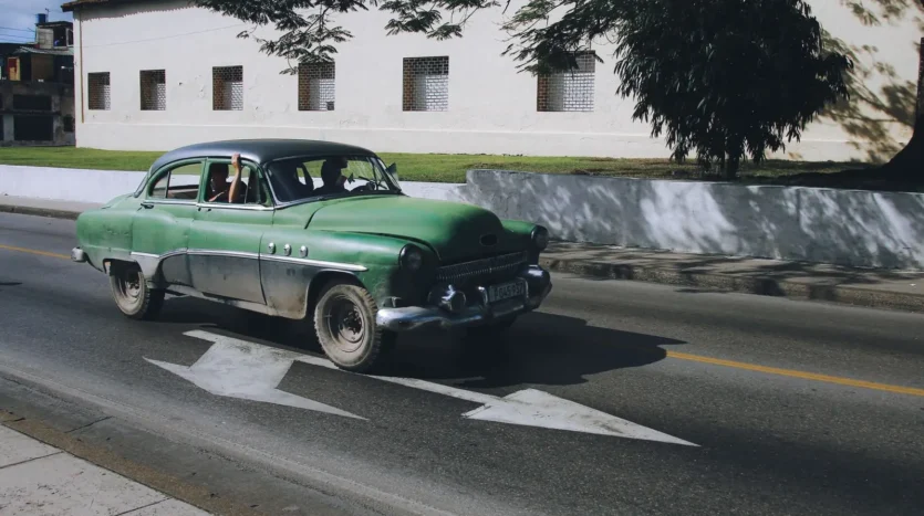 Green classic car driving down a street under a blue sky