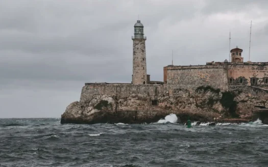 Waves beside the Morro Castle and its lighthouse in Havana under a gray sky