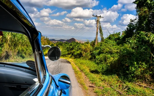 Classic car driving along a rural road among vegetation