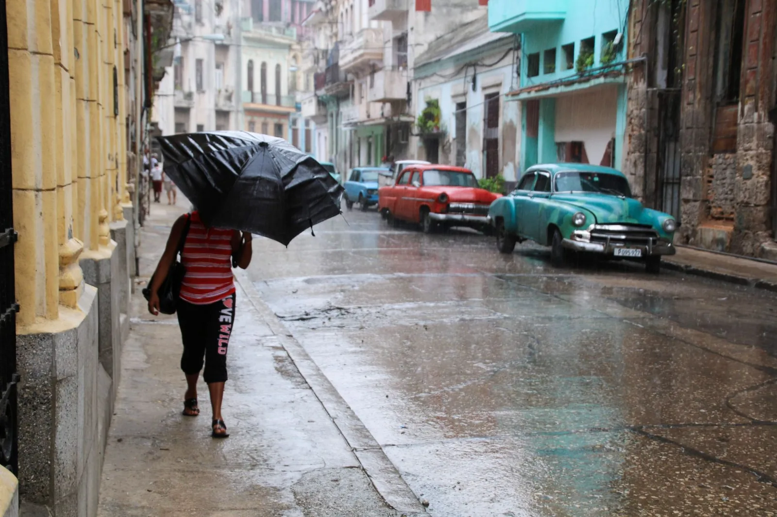 Mujer con paraguas caminando por una calle mojada de La Habana con coches antiguos